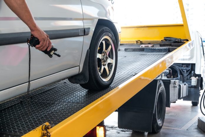 Closeup on car towed onto flatbed tow truck with cable