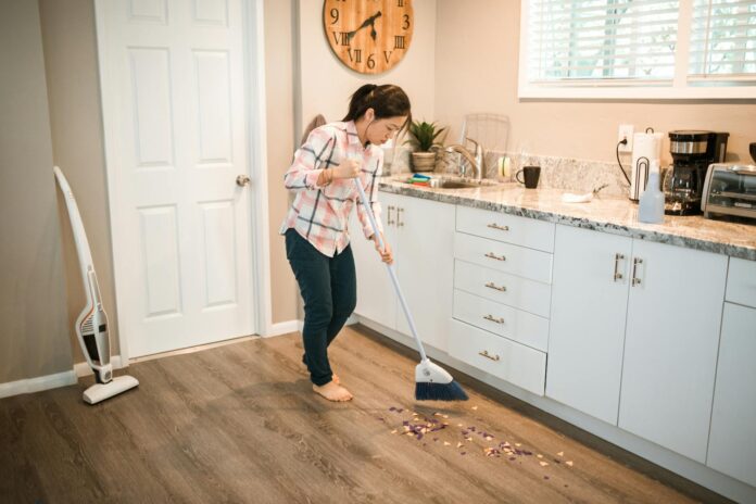 photograph of a woman in a plaid shirt sweeping with a white broom