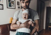 man in gray carrying a sleepy baby