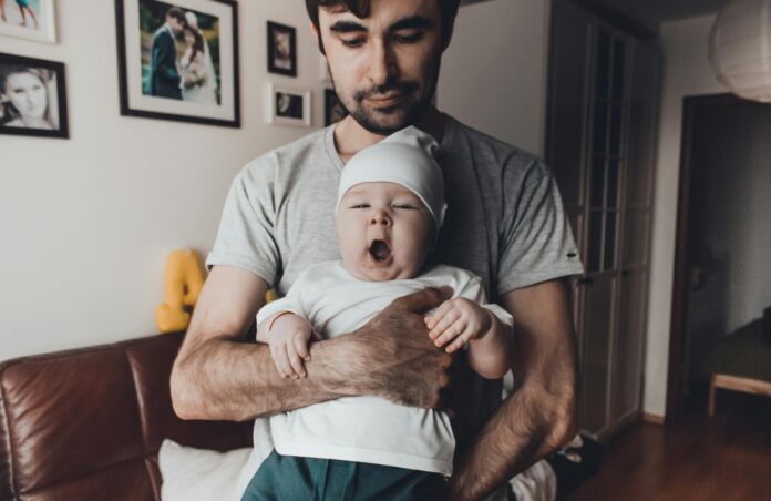 man in gray carrying a sleepy baby