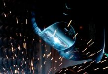 person in welding mask while welding a metal bar