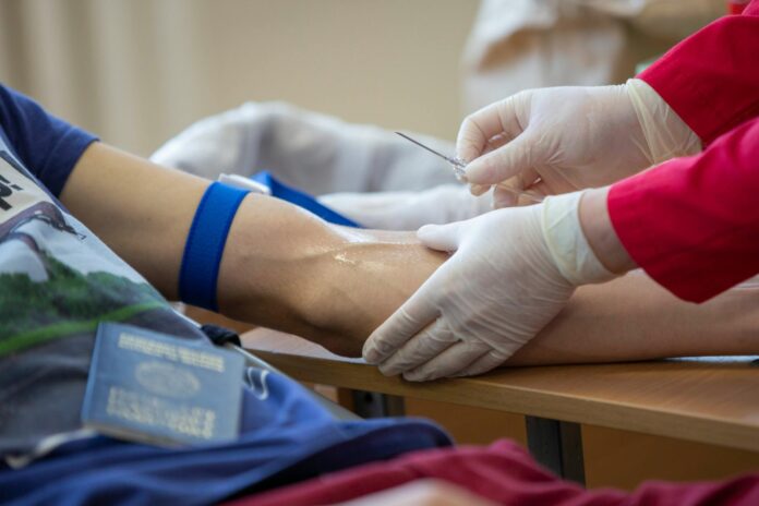 medical practitioner taking a blood sample from a womans hand