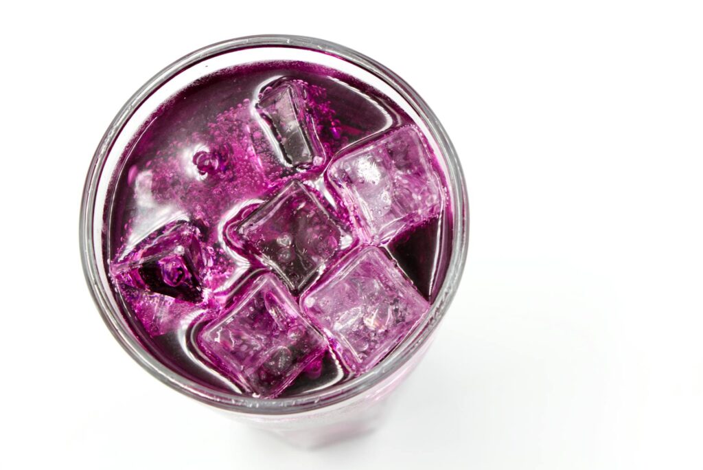 a purple colored drink with ice cubes in a glass