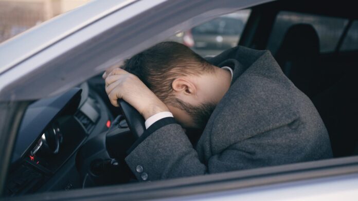 stressed man in car resting on steering wheel
